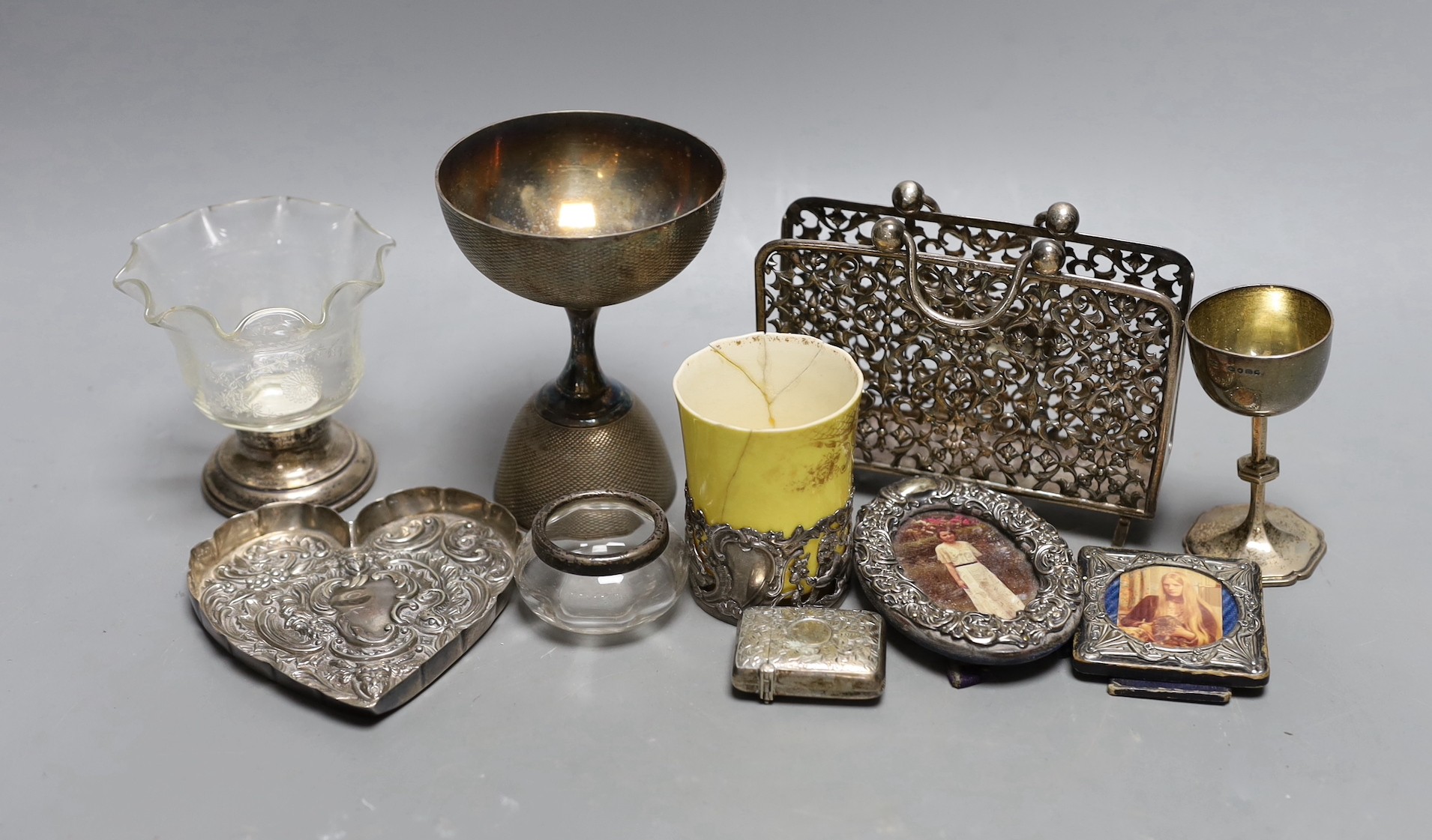 A small group of collectable items including a silver stationary rack, Laurence Emanuel, Birmingham, 1901, height 9.7cm, a silver communion goblet, silver mounted porcelain coffee cup, silver mounted glass vase, silver v